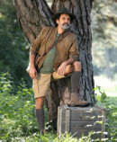 Man wears Juzo Adventure in poppy and stands in the meadow by a tree