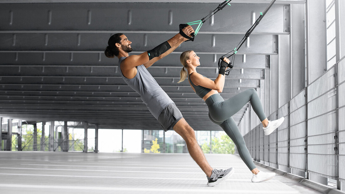 Um homem e uma mulher treinam numa garagem subterrânea com uma fita TRX