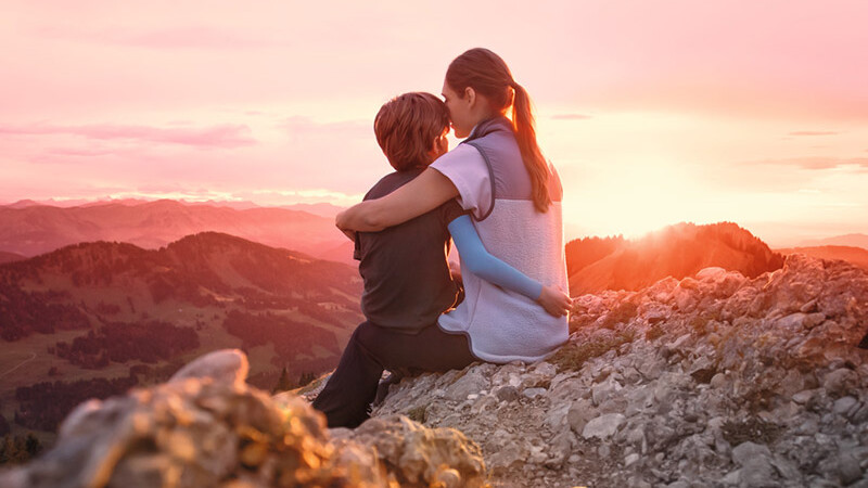 Una madre está sentada con su hijo en la cima de una montaña. El niño lleva una manga de compresión.
