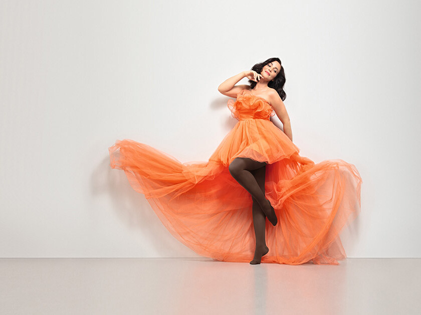 Frau in orangenem Kleid. Sie trägt den Juzo Inspiration als braune Strumpfhose