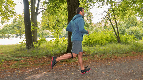 Mann joggt durch Wald und trägt ein Patellasehnenband