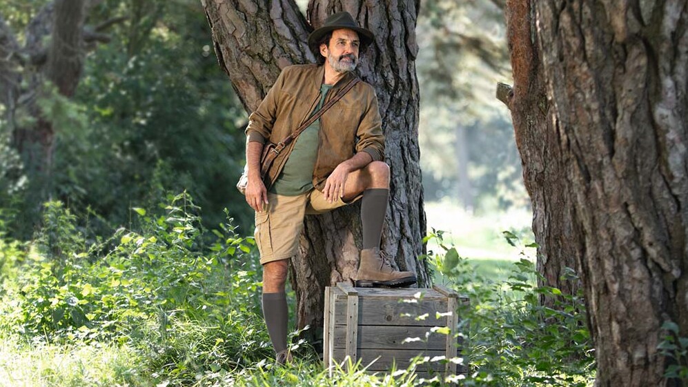 Ein Mann mit Entdecker-Outfit steht in der Natur und schaut in die Ferne. Er trägt kniehohe Kompressionsstrümpfe. Ein Mann mit Entdecker-Outfit steht in der Natur und schaut in die Ferne. Er trägt kniehohe Kompressionsstrümpfe.